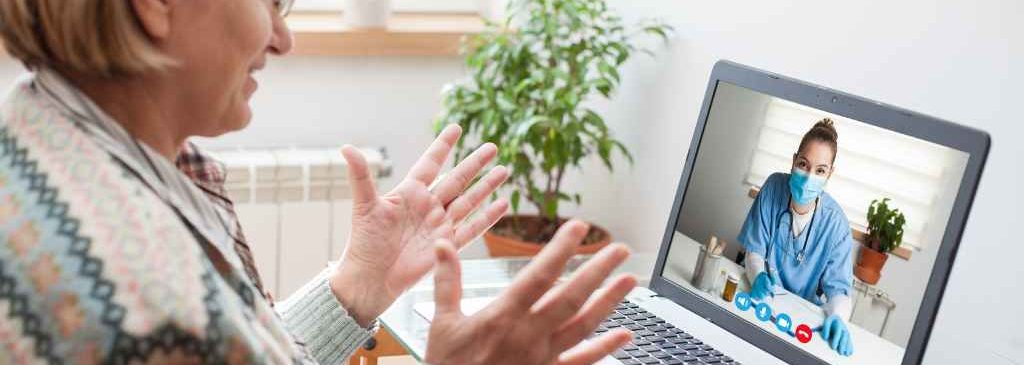 Donna anziana durante una video consulenza con fisioterapista, seduta di teleriabilitazione a distanza tramite computer portatile